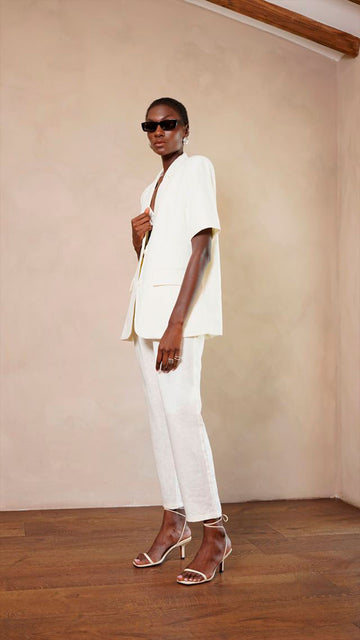 Woman in a white outfit standing against a beige wall.