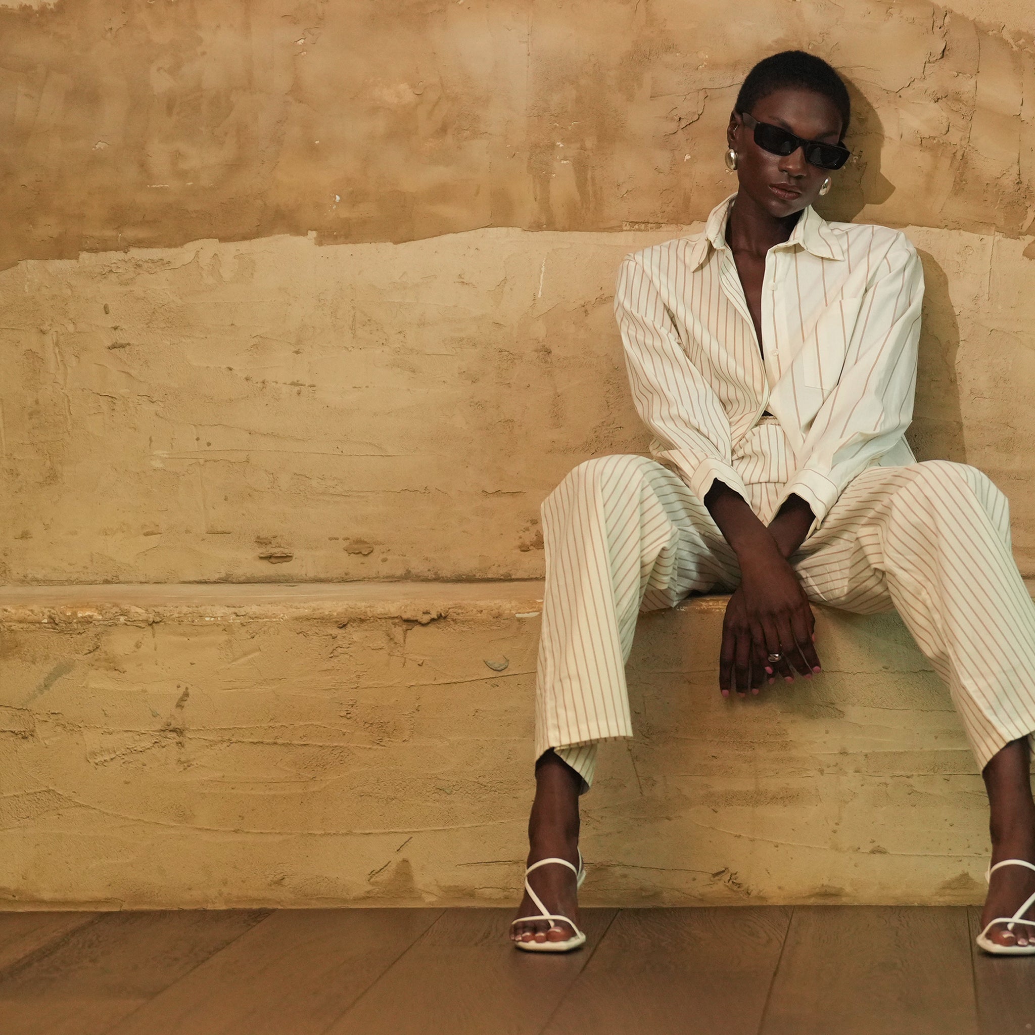 Person wearing a white outfit sitting on a textured beige wall.