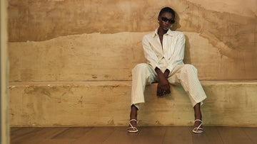 Person wearing a white outfit sitting on a textured beige wall.